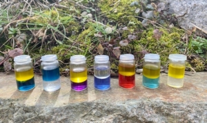 verschieden farbige durchsichtige Wasser und Oelmischungen auf einem Stein in der Natur