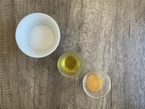 Eine Schale mit Zucker ein glas mit Öl und ein Glas mit getrockneten Mandarinenschalen