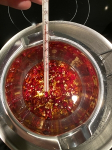 rote geschnittene Chillischoten in Öl in einem Wasserbad mit Thermometer