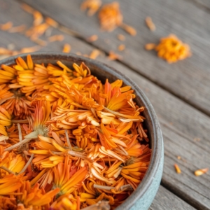 a-photo-of-a-bowl-filled-with-calendula-_ge5d7yBKSwG2ON8pTeywmg_sORhQ9LXSleE2CbRNEC8lg getrocknete orange Ringelblumenblten in einer grauen Schale auf Holz