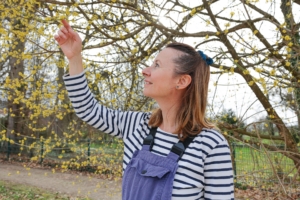 Frau steht in einem Garten und schaut die Blüten eines Baumes an.